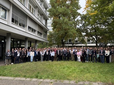Großes Gruppenfoto von Menschen vor einem Bürogebäude und Bäumen im Freien.